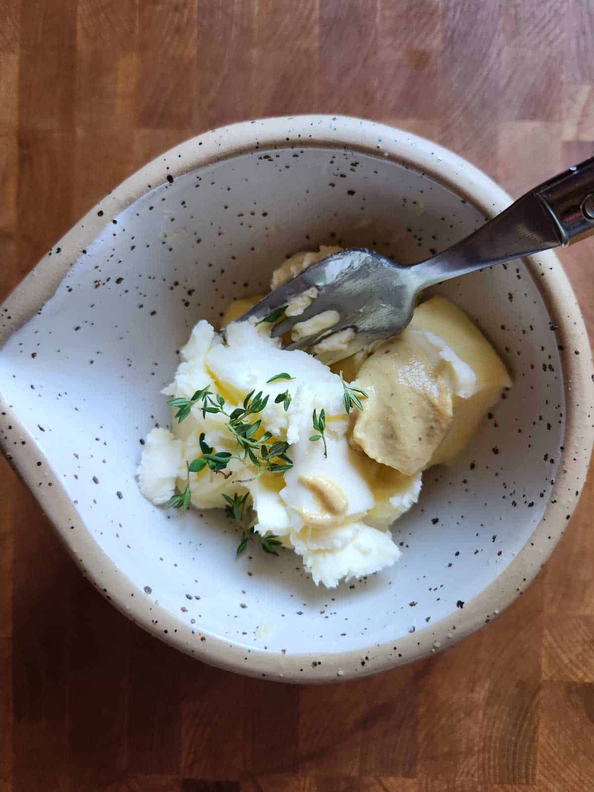 Butter, herbs and seasoning in a beige bowl with with a fork.