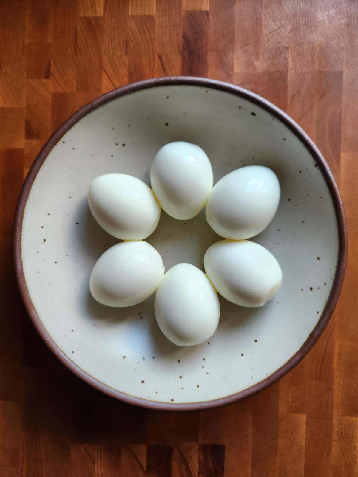 Overhead of six peeled hard-boiled eggs in a bowl.