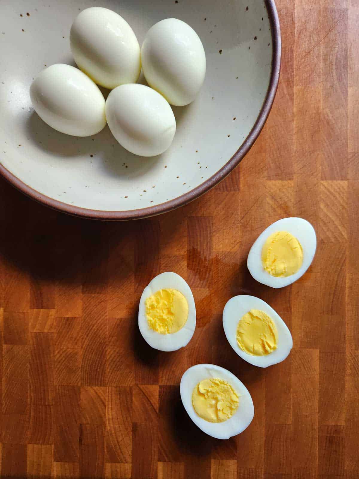 Hard boiled eggs sliced open on a wood cutting board.