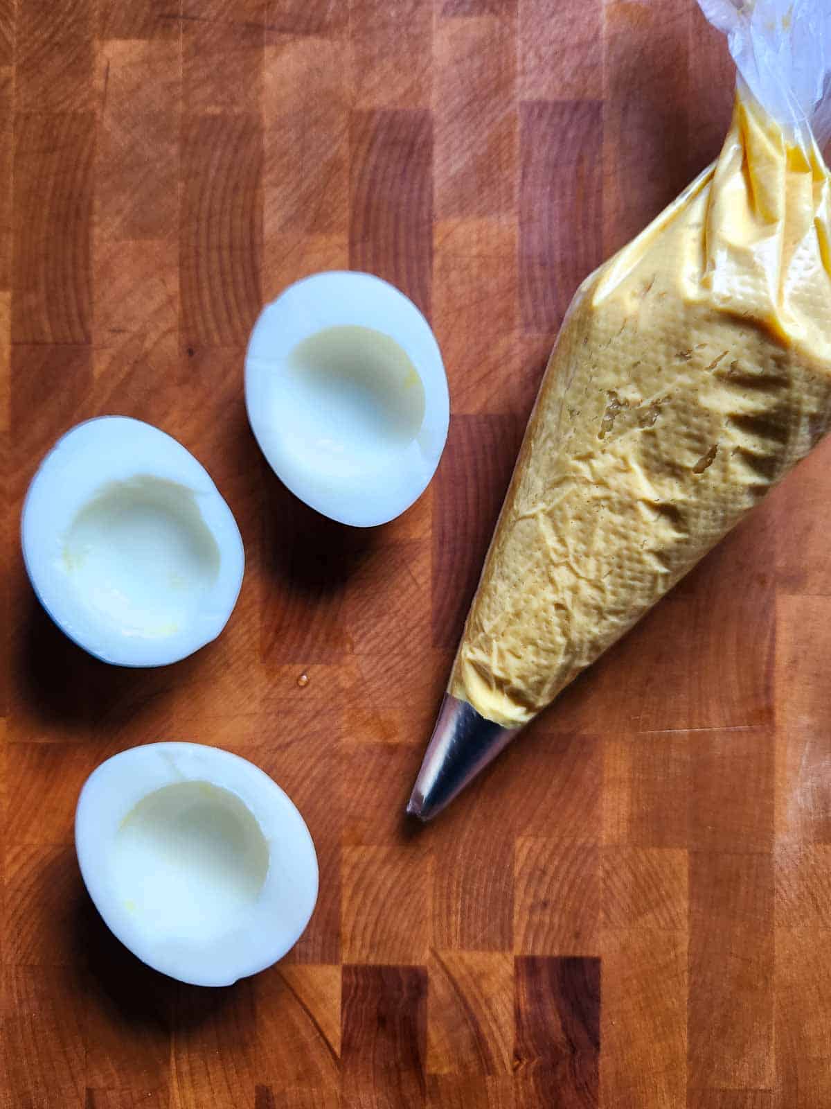 Deviled egg filling in a piping bag with 3 egg halves on the side.