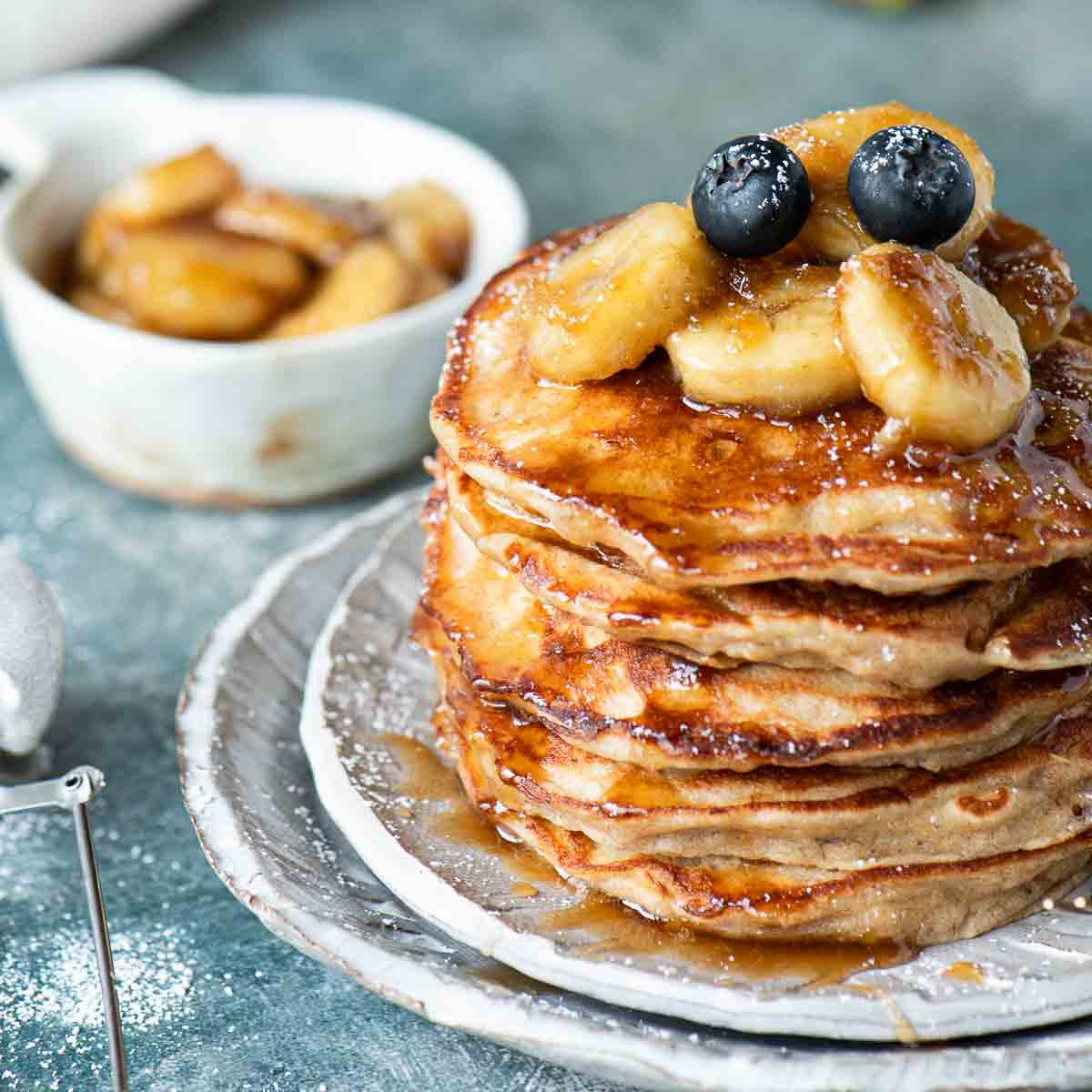A stack of banana pancakes with bananas on top on a white plate.