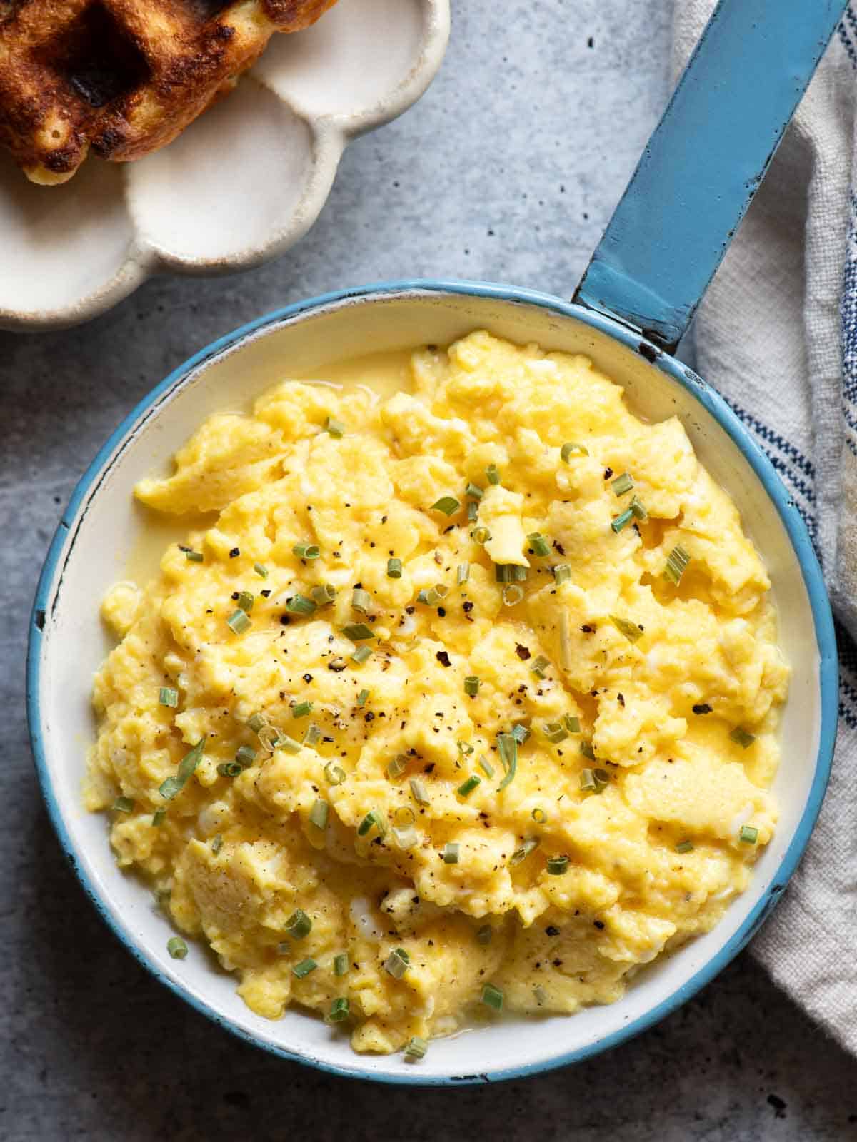 Overhead of buttermilk scrambled eggs in a blue skillet.