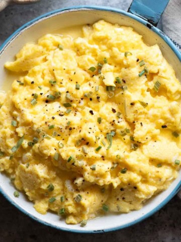 Overhead close up of scrambled eggs in a blue skillet.