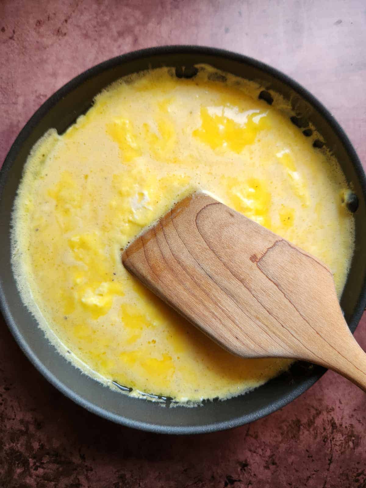 Scrambled eggs in a pan with a wooden spoon.