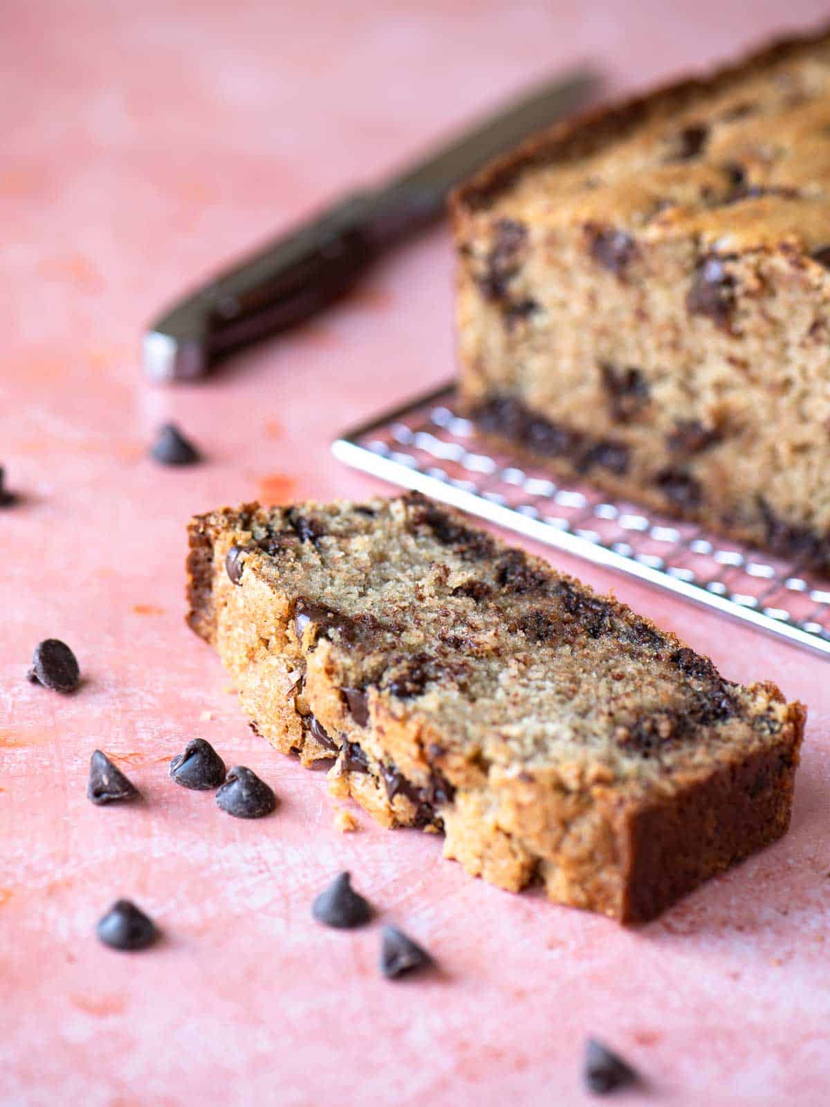Eye level slice of chocolate chip loaf on a pink surface.