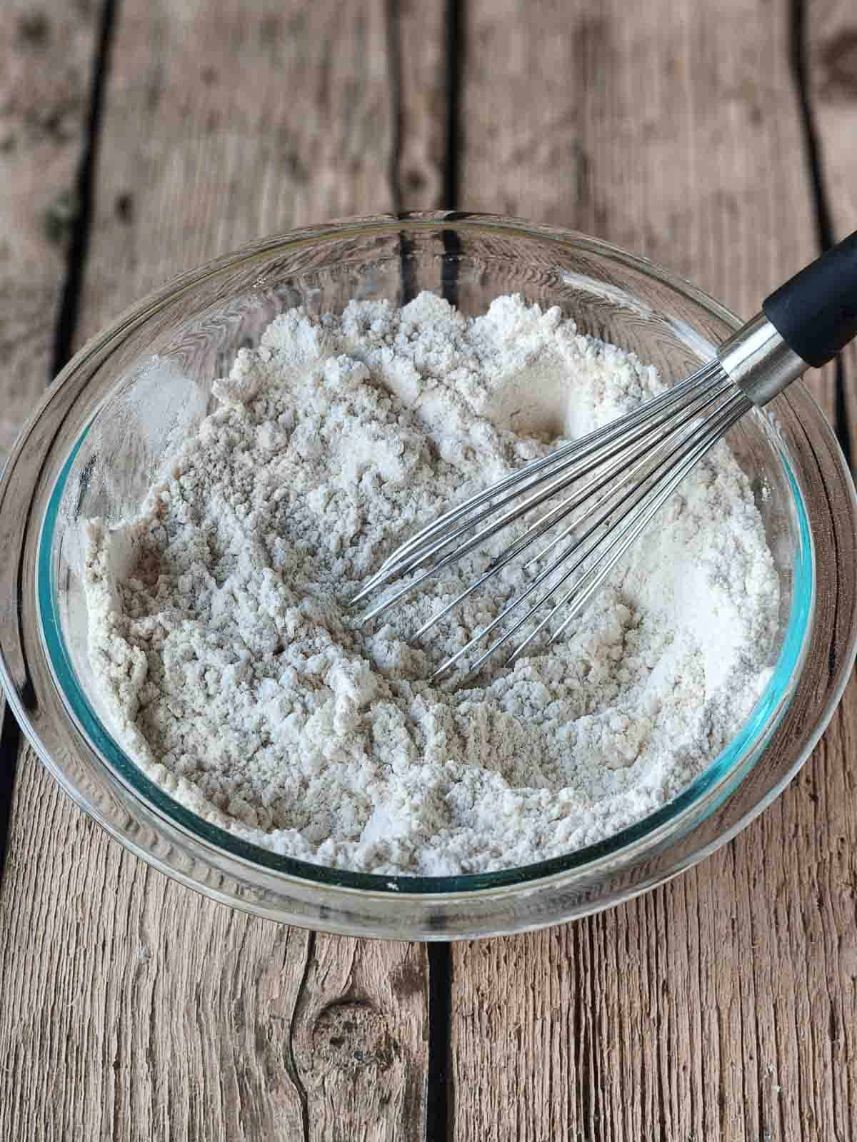 Dry ingredients in a clear bowl with a whisk in it.