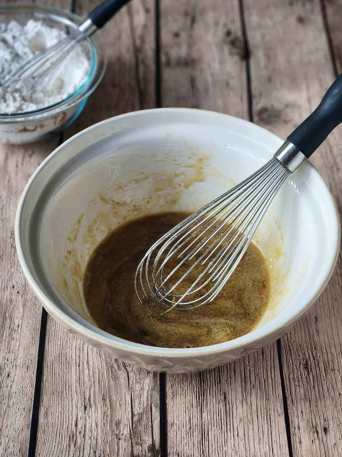 Wet ingredients in a large mixing bowl with a whisk in it.