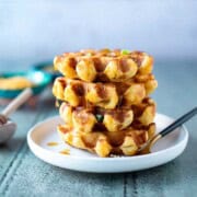 Stack of green chili cheddar waffles with honey dripping down them.