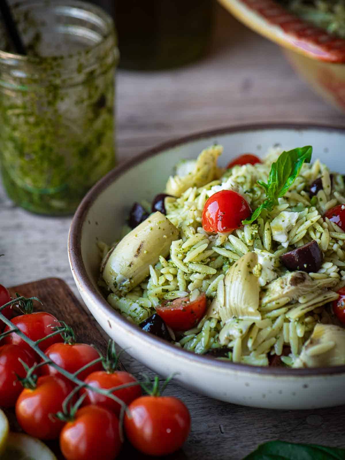 Close up of orzo pesto salad with cherry tomatoes on the side.