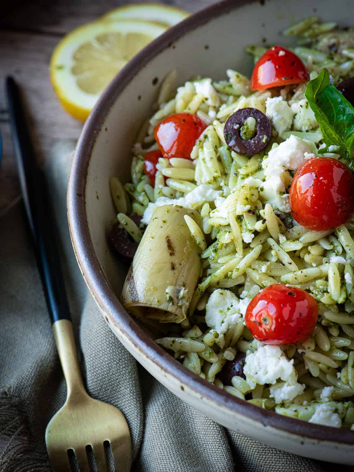 Angled view of pesto salad with pesto and tomatoes with a fork next to it.