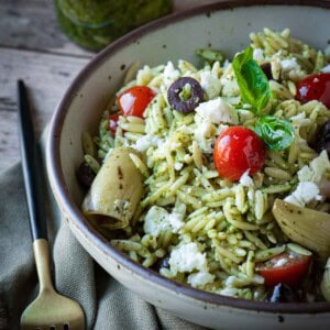 Close up of pesto salad in a beige bowl on a wood surface.