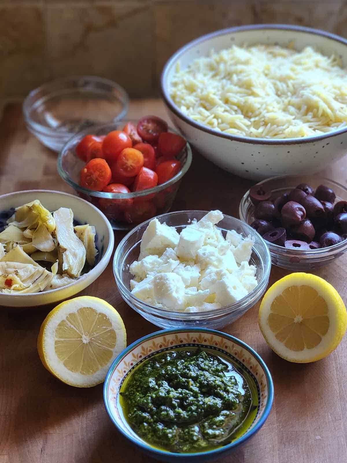 Ingredients for orzo pasta salad on a wooden board.