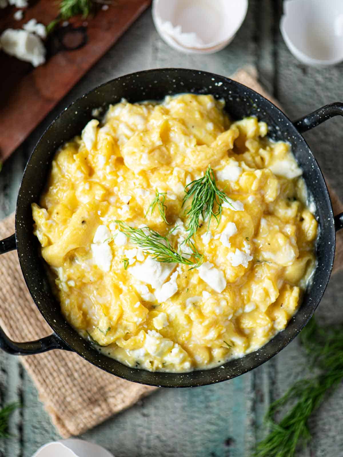 Overhead of scrambled eggs in a black skillet with dill on top.