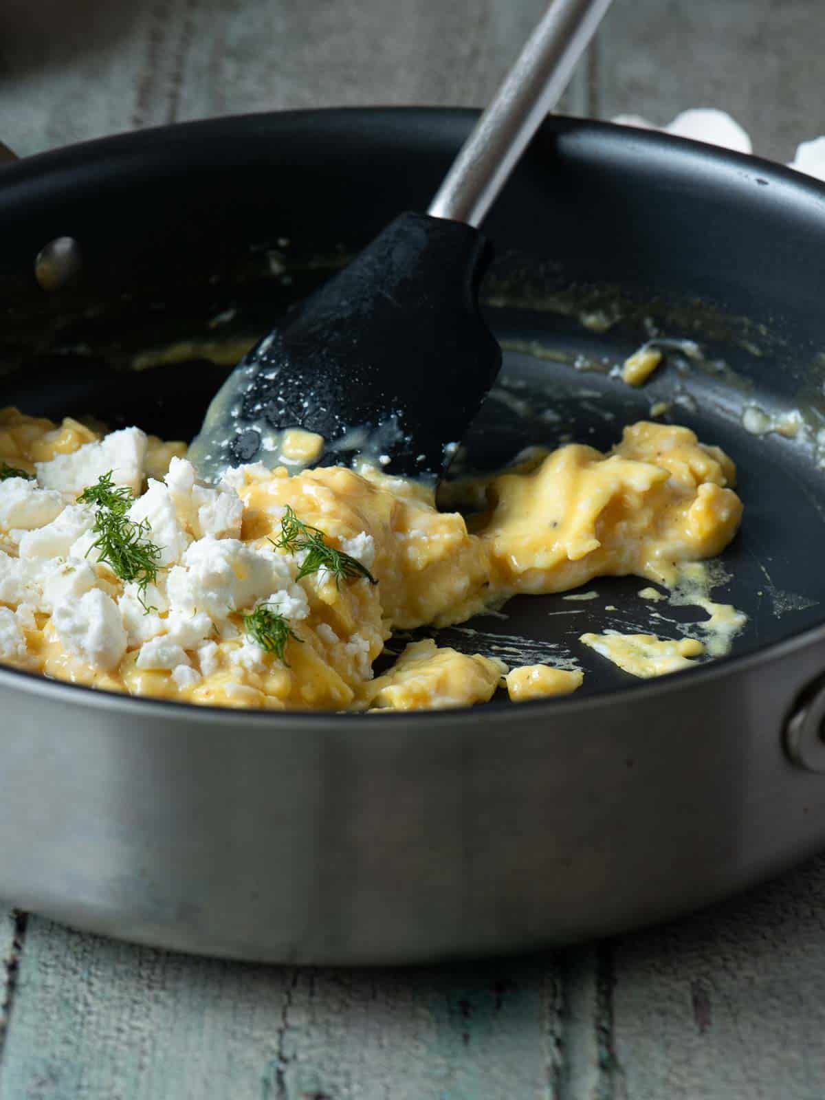 Scrambled eggs being prepared in a skillet with a spatula and toppings.