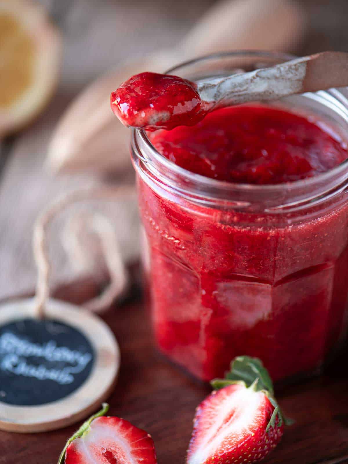 Close up of a spoon dipped into strawberry jam in a clear jar.
