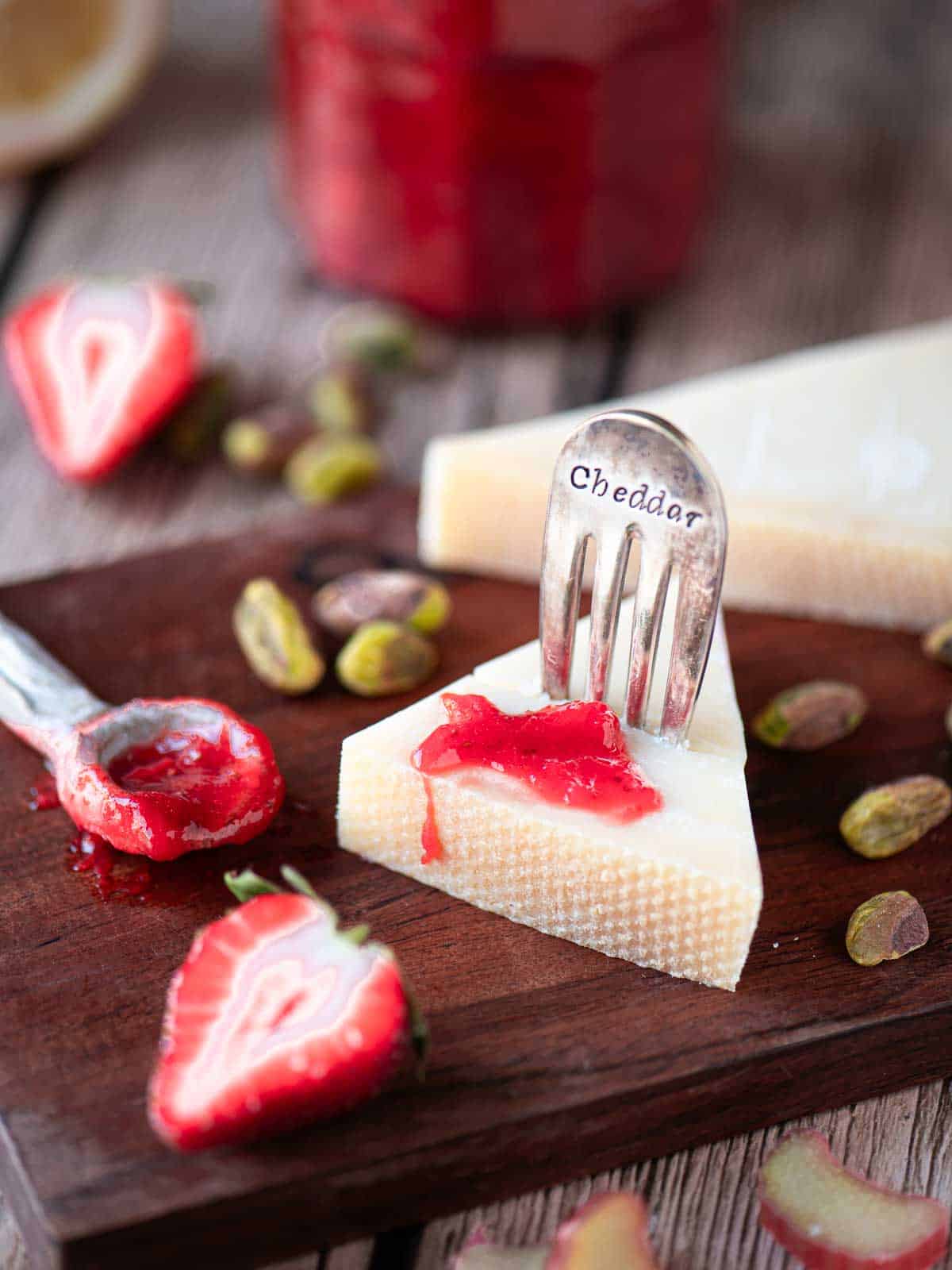 Strawberry rhubarb jam on a wedge of cheese on a wooden board.