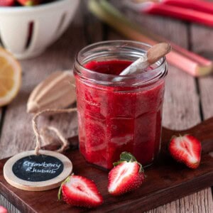 Strawberry rhubarb jam on a wood board with fruit scattered around it.