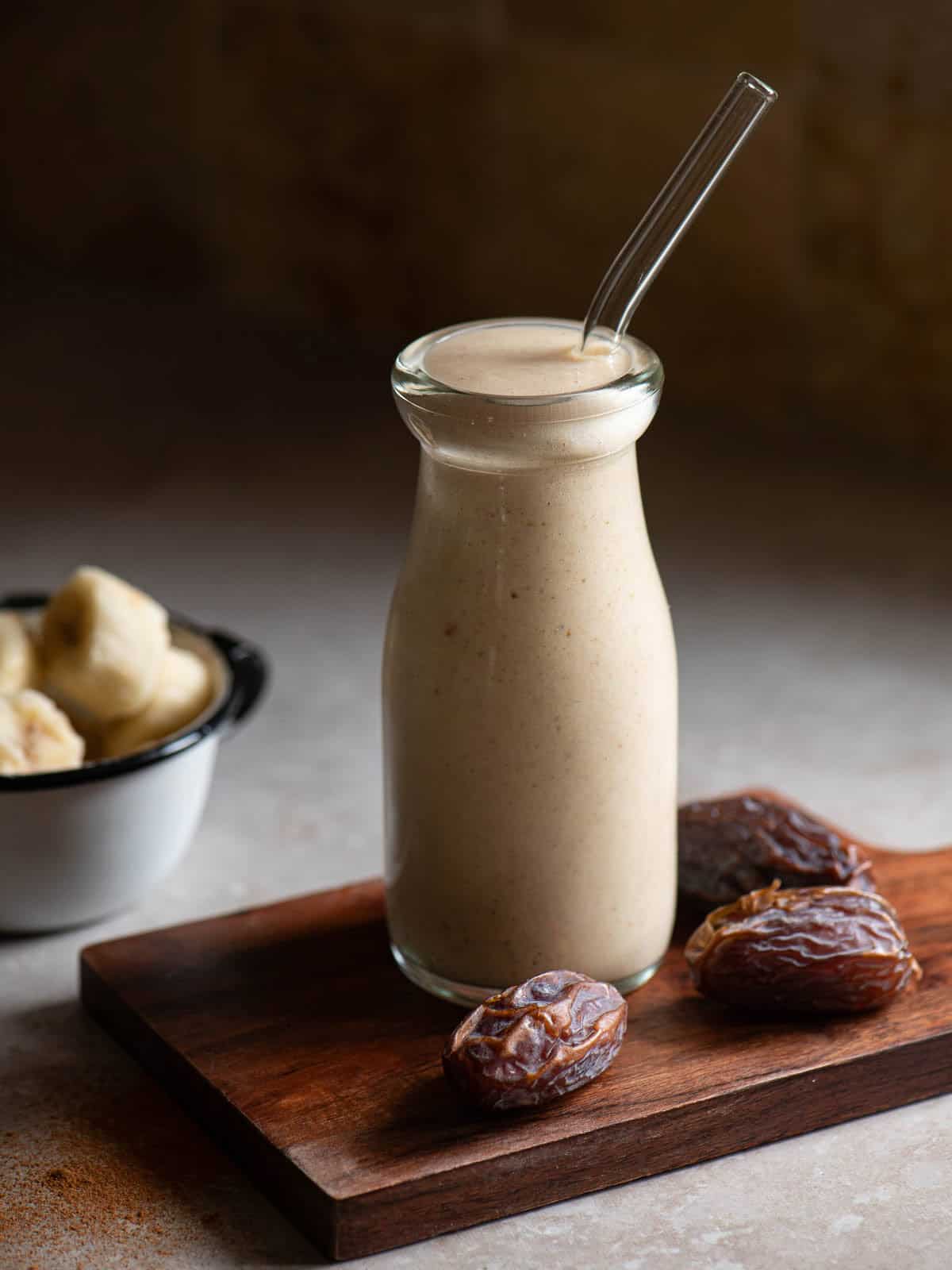 Date smoothie in a clear glass with a clear straw.
