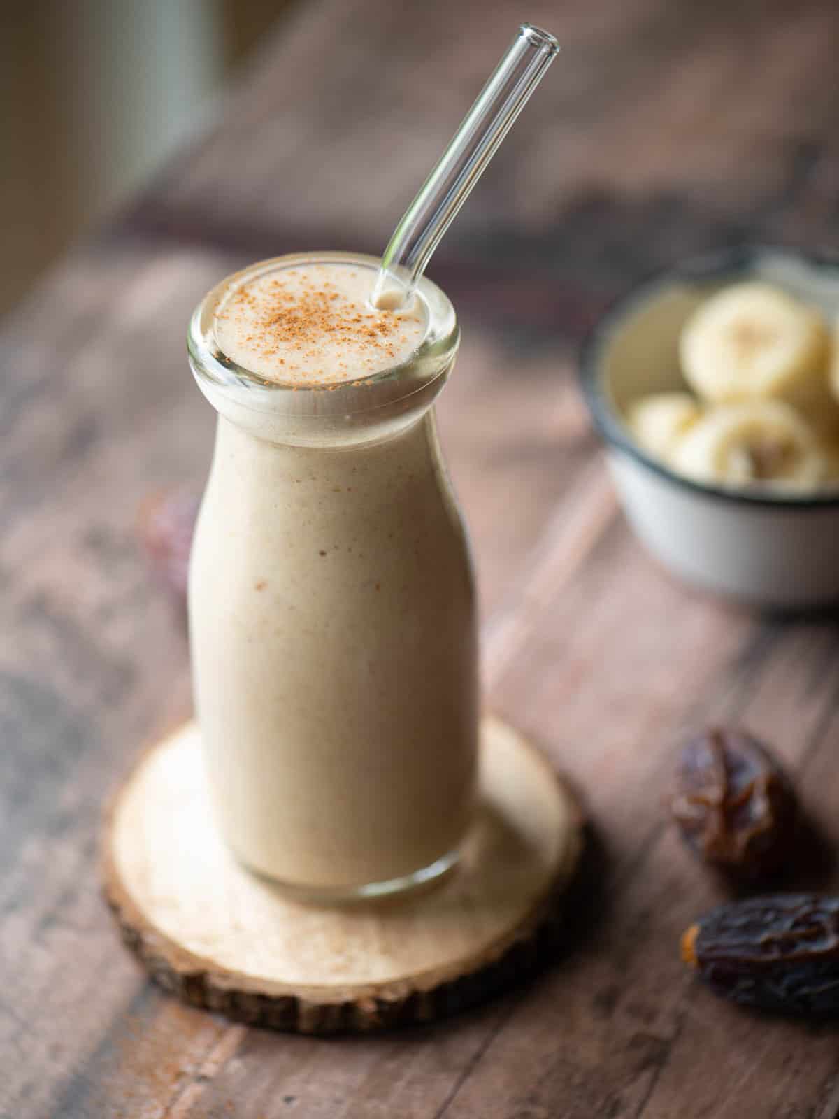 Angled view of a banana smoothie with a straw in it.