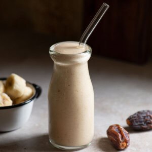 Close up of a banana smoothie in a clear jug with a straw.