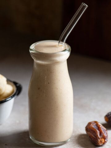 Close up of a banana smoothie in a clear jug with a straw.