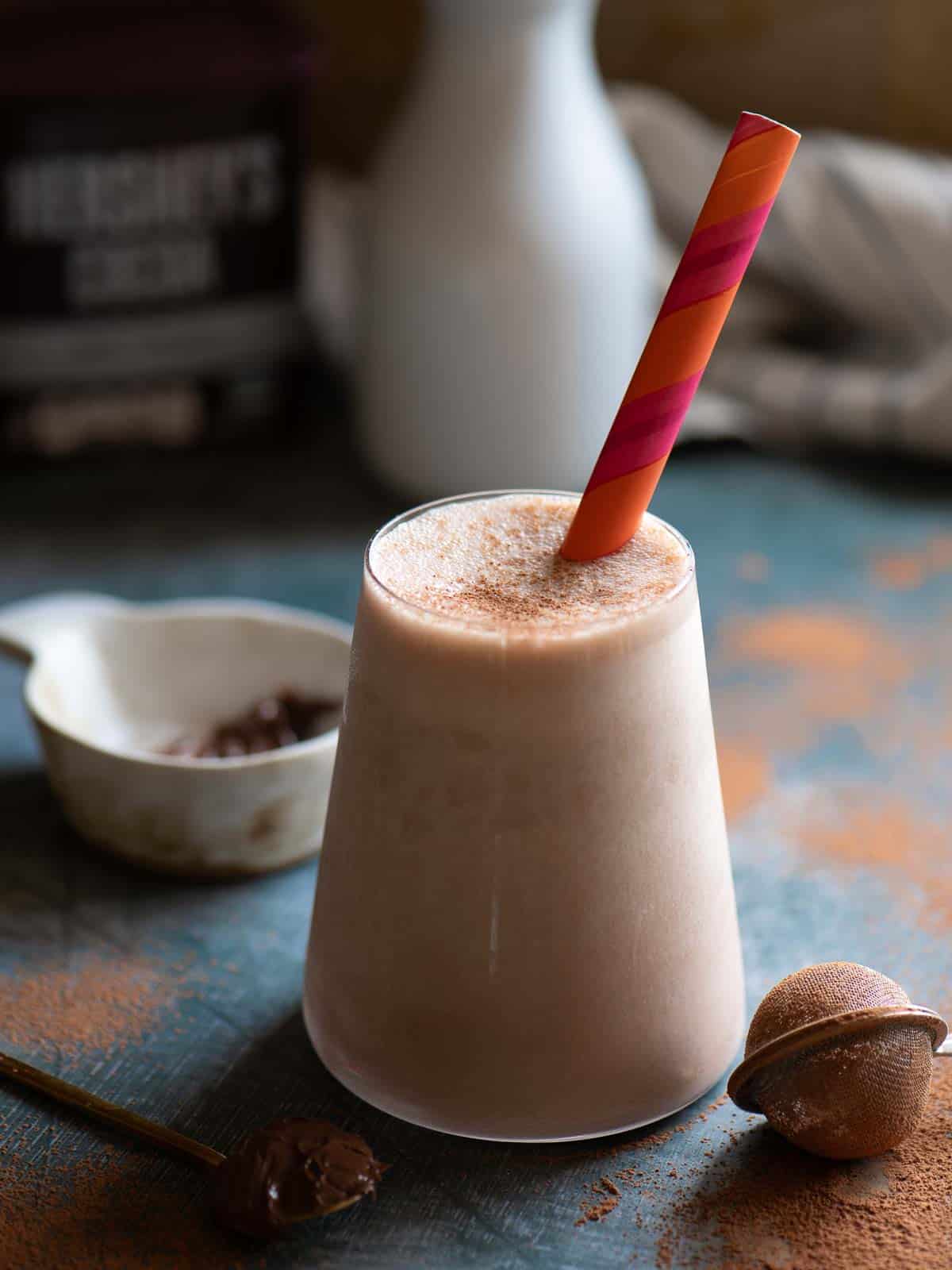 Chocolate smoothie in a tall clear glass with an orange straw.