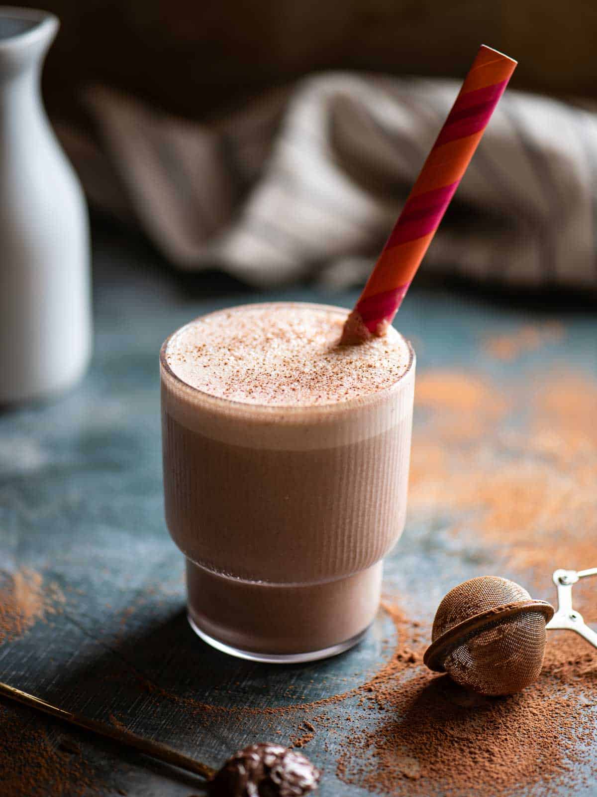 Tahini oat milk smoothie in a ribbed glass with an orange striped straw.