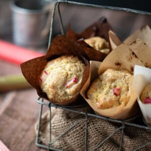 Rhubarb muffins in a metal basket with stalks of rhubarb to the side.
