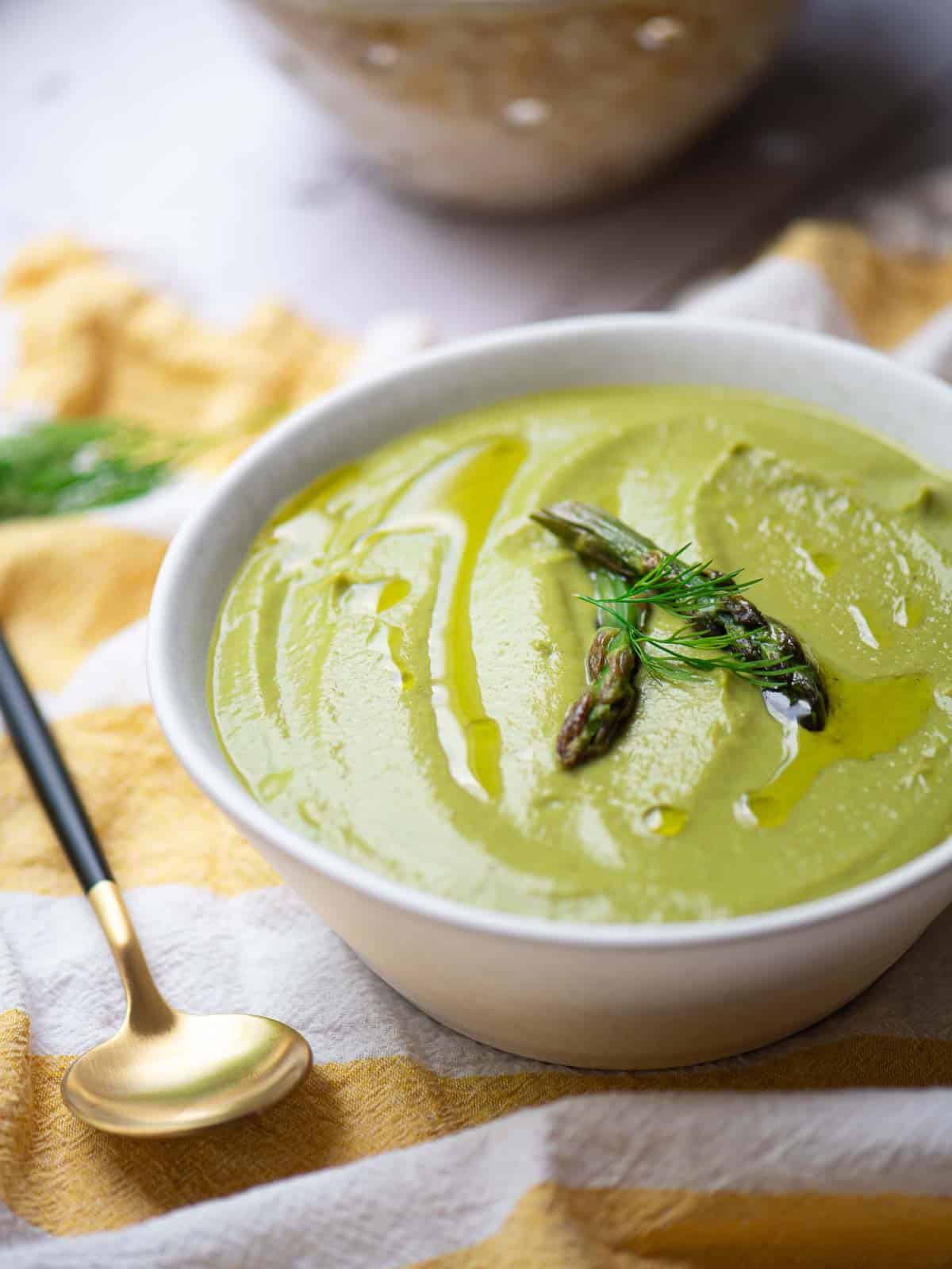 Close up of asparagus leek soup in a white bowl over a yellow striped linen.