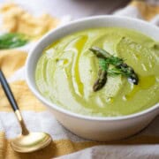 Close up of asparagus leek soup in a white bowl over a yellow striped linen.