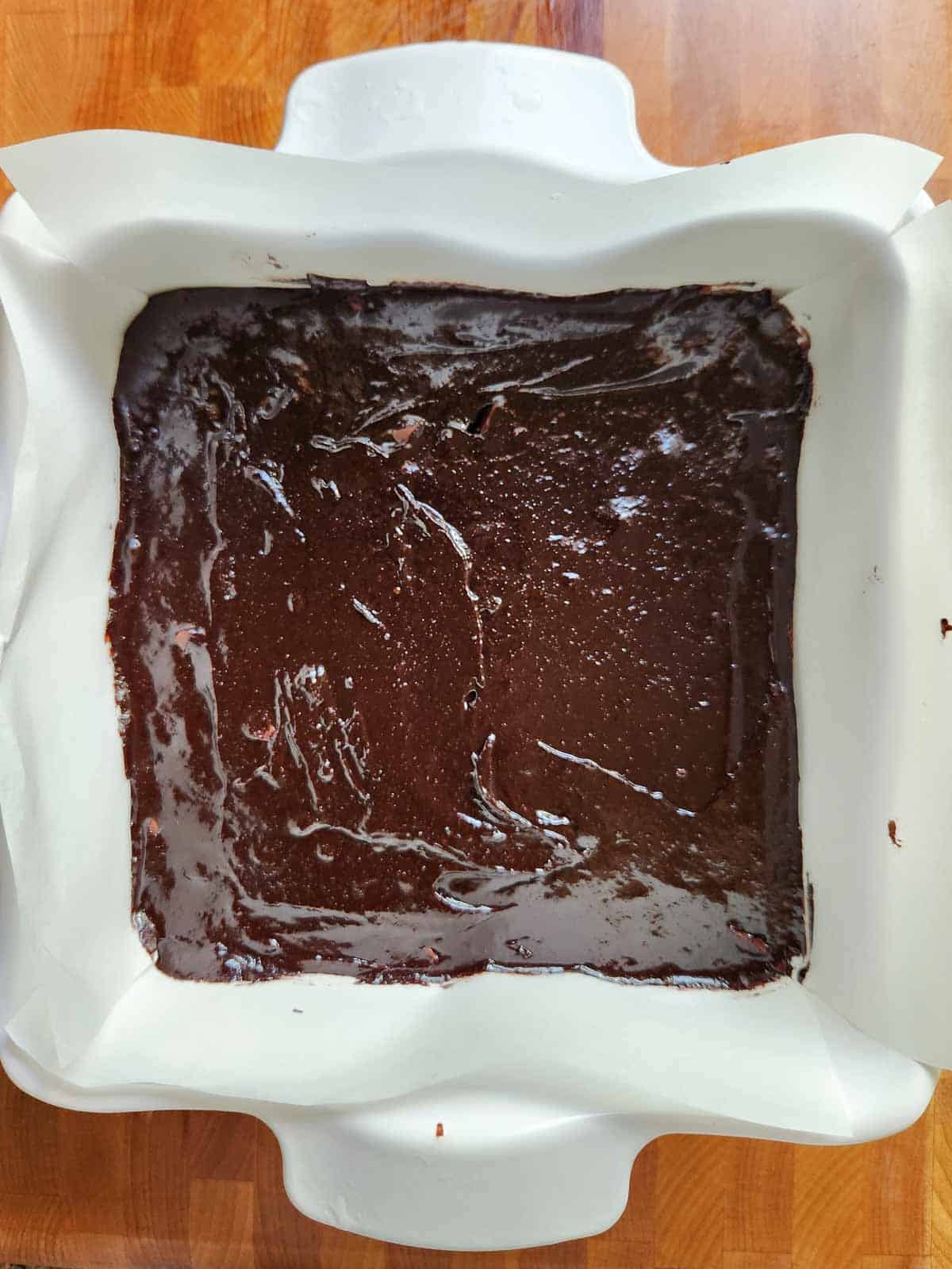 Brownie batter in a white ceramic square pan ready for baking.