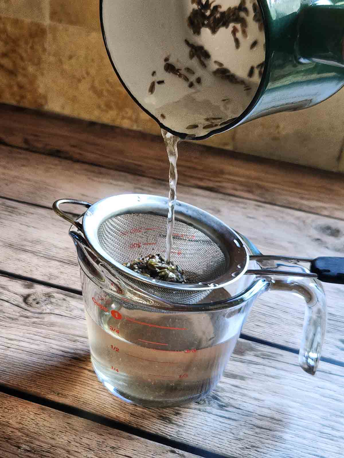 Straining lavender simple syrup into a clear glass.