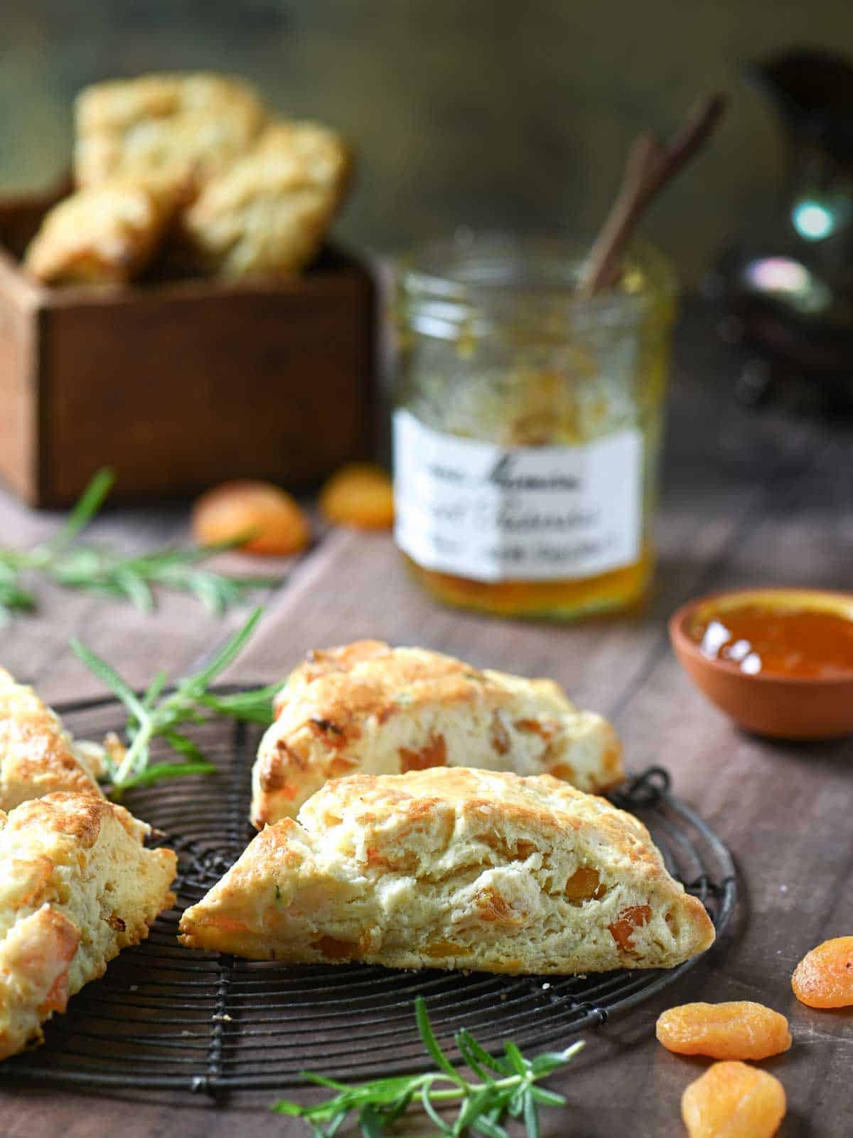 Scones on a wire rack with jam and apricots in the background.