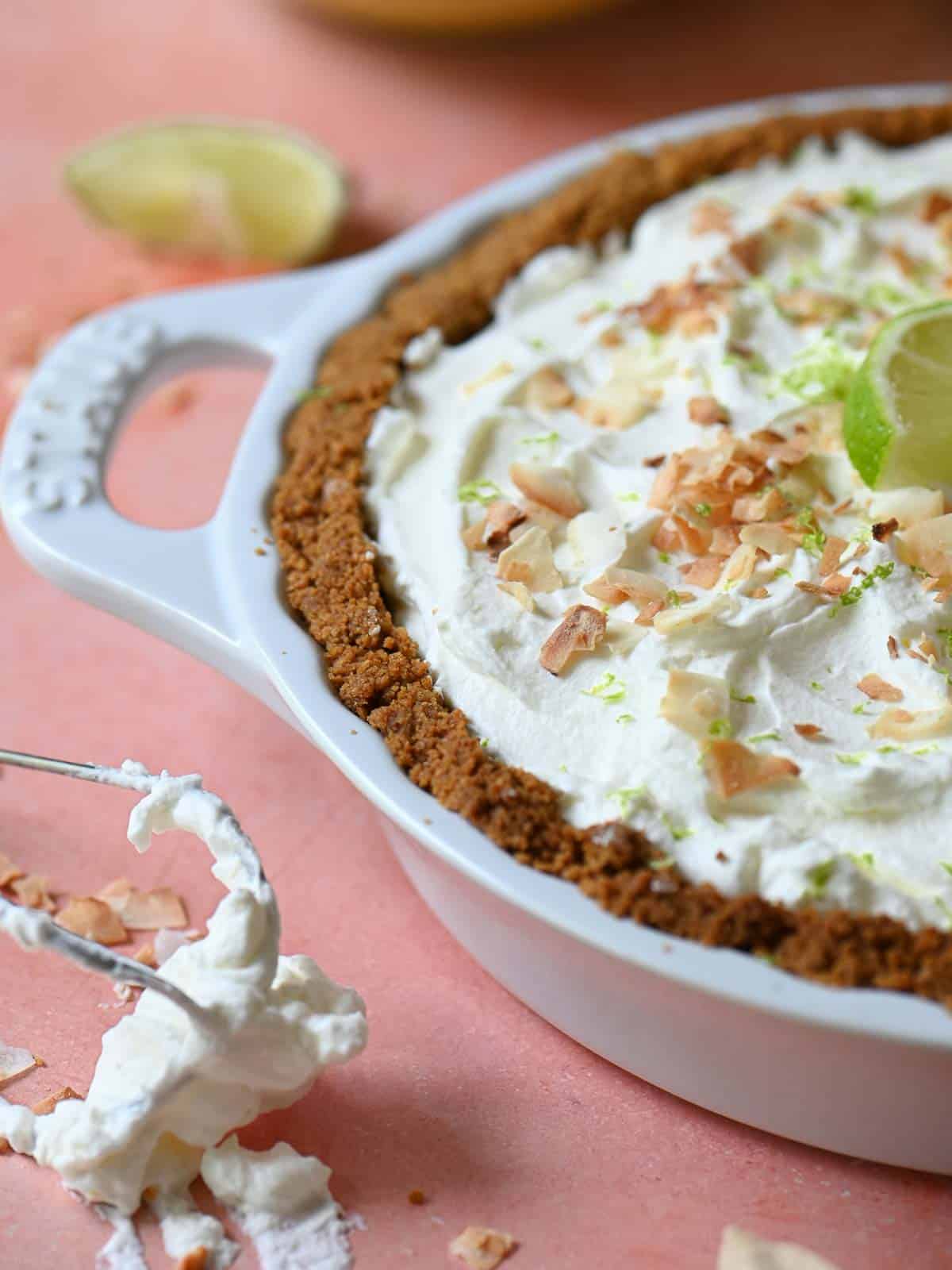 Close-up of coconut key lime pie on a pink surface with limes.