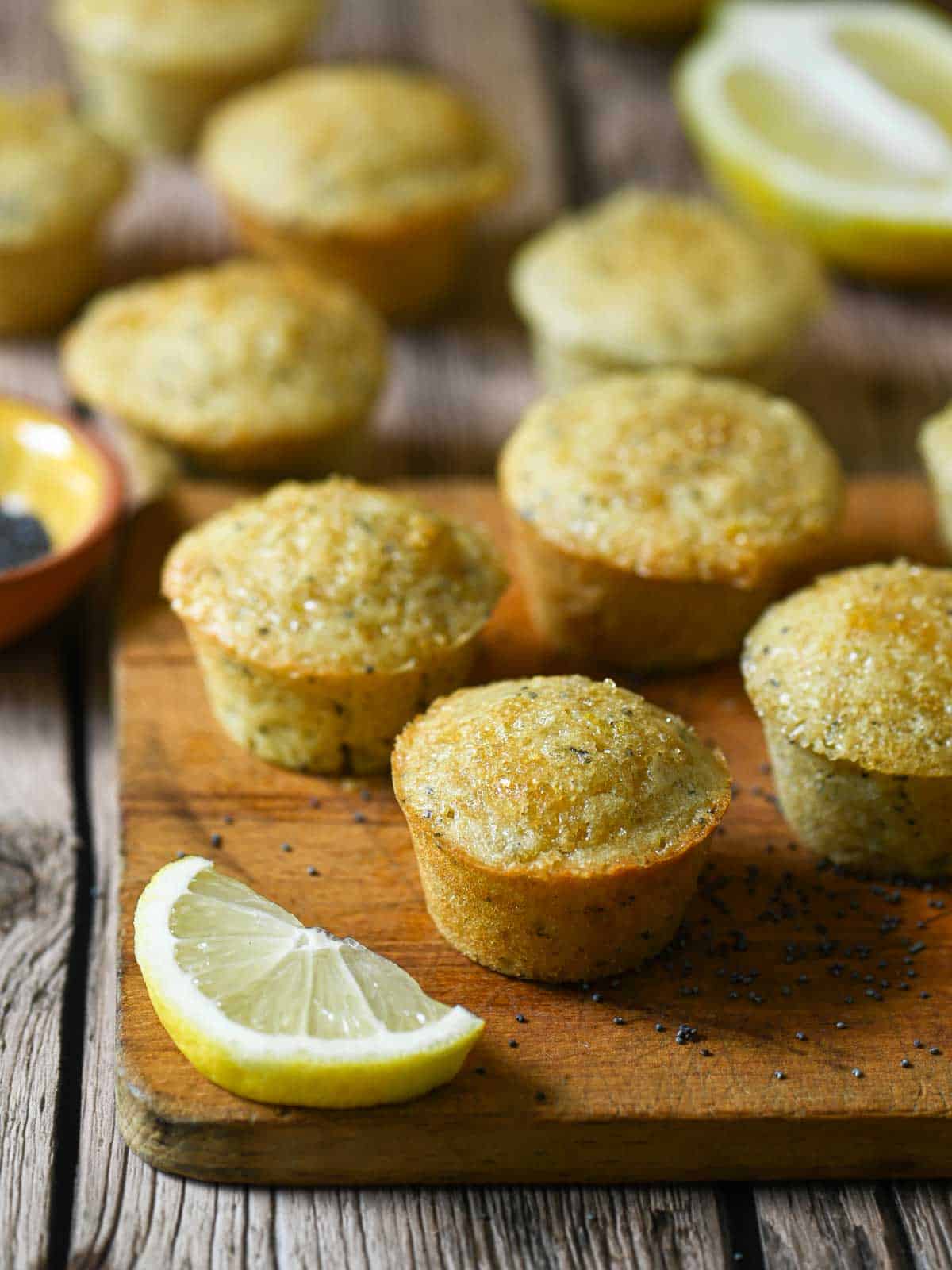 Mini lemon poppy seed muffins on a wood board with a lemon wedge.