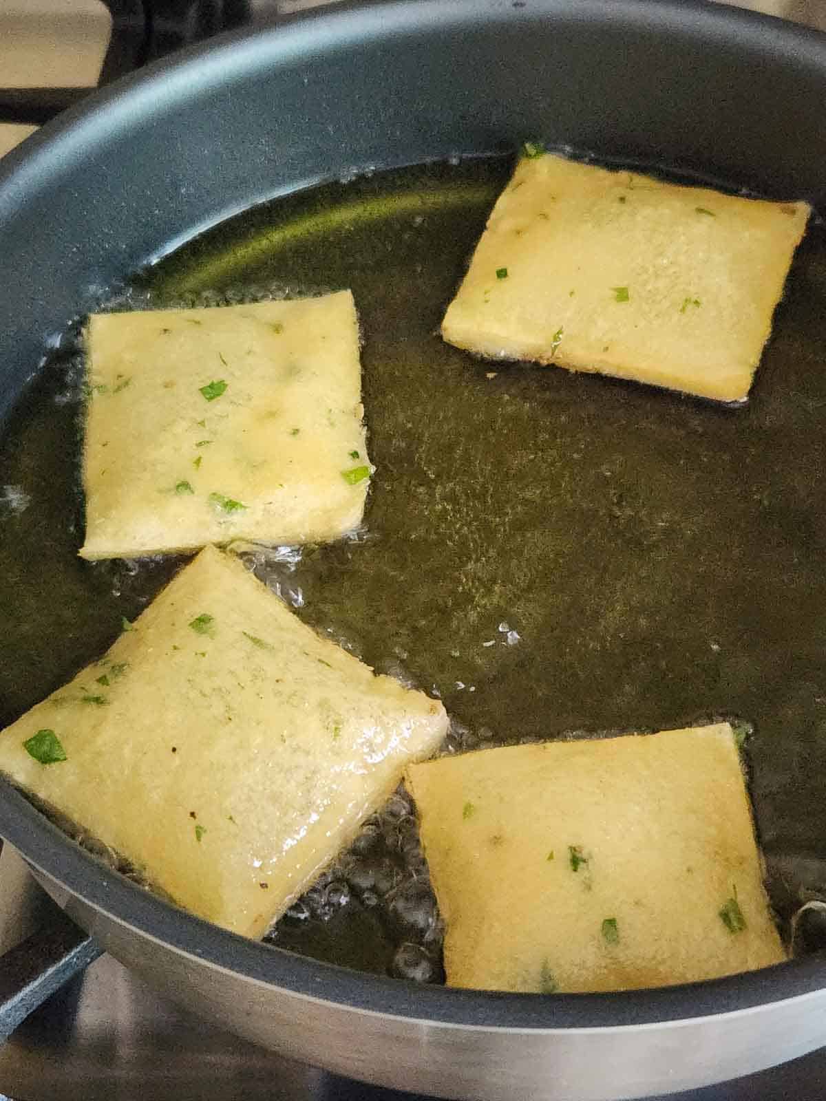 Panelle frying in a pan of oil.
