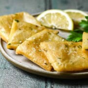 Close-up of panelle on a beige plate with lemon wedges.