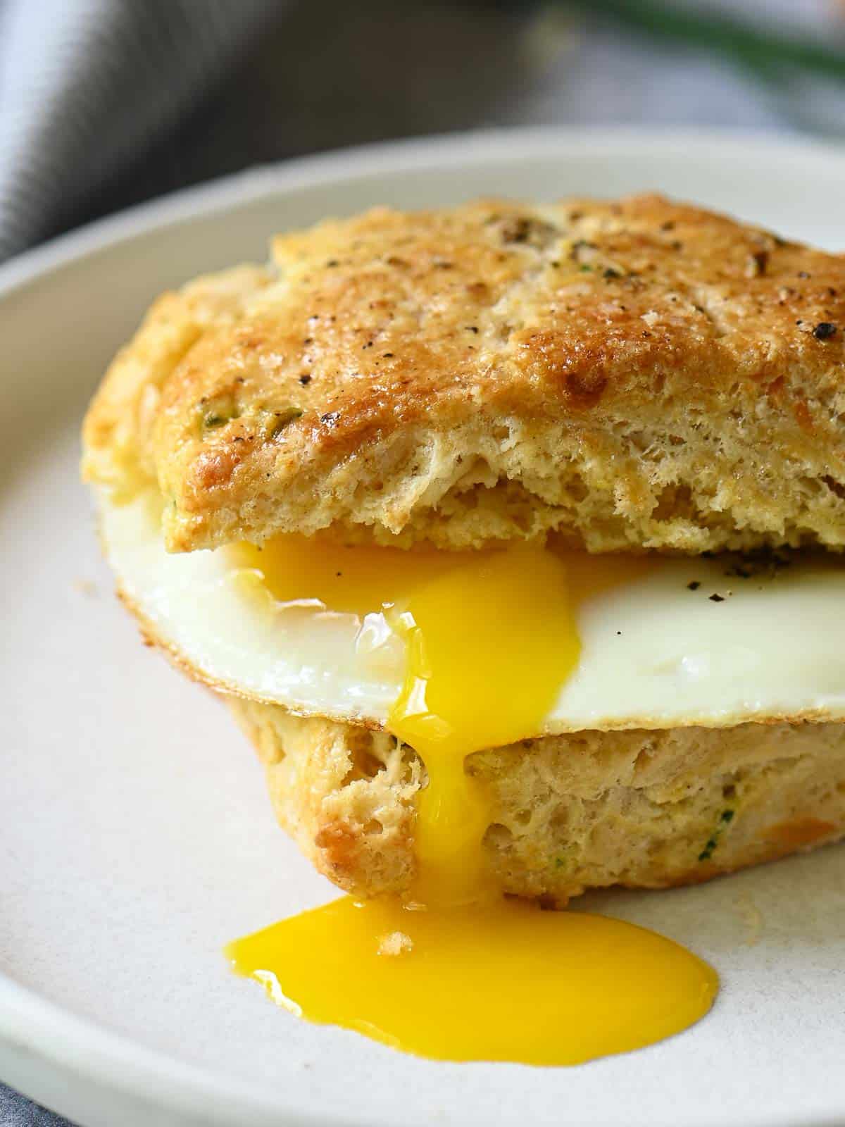 Drippy fried egg inside a savory scone on a white plate.