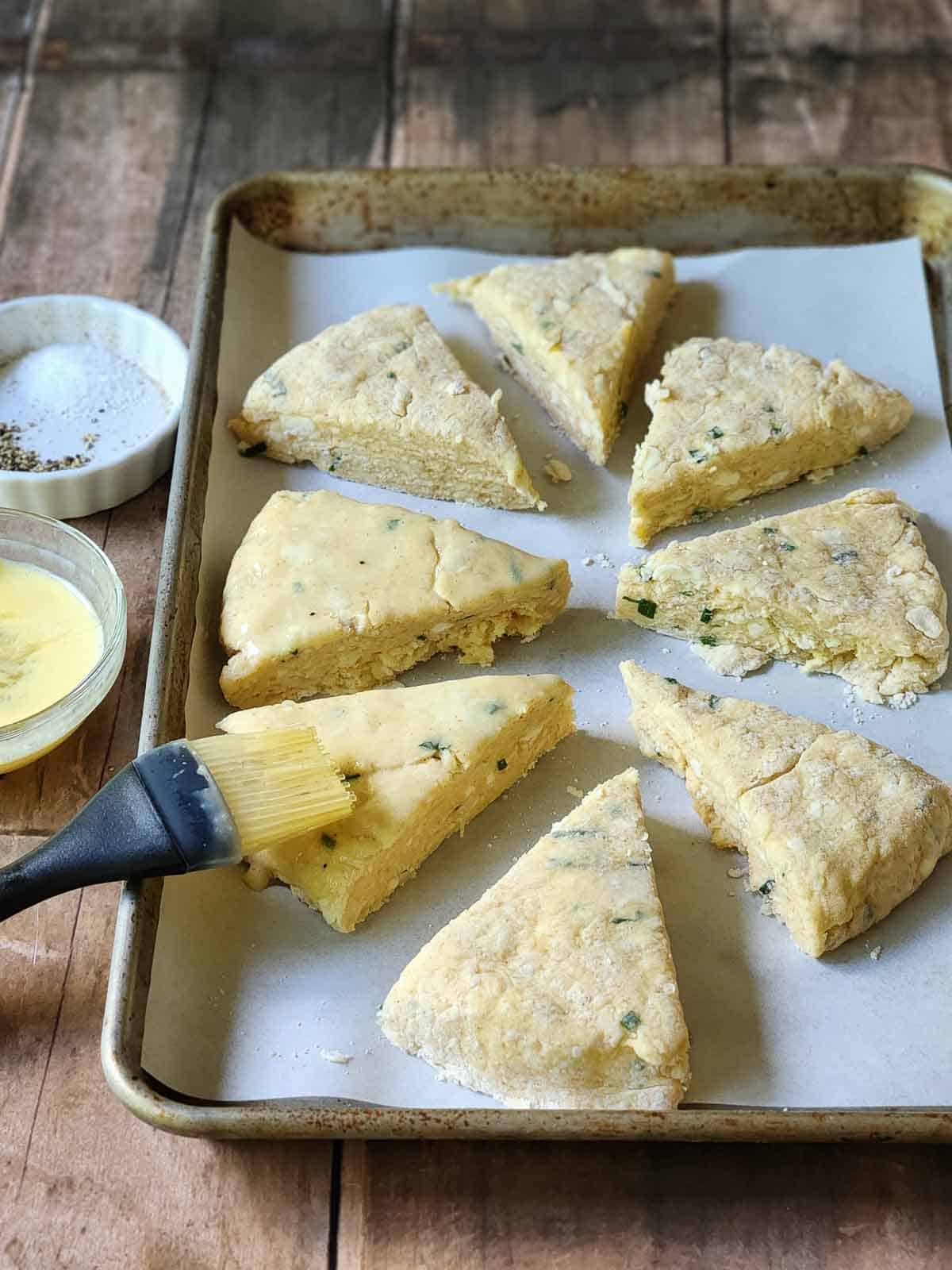 Egg washed being brushed onto scones in a baking pan.