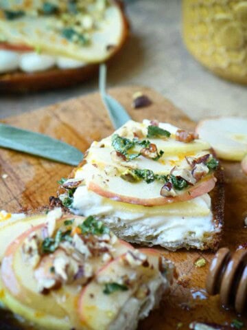 Apple toast sliced open on a cutting board with sage and honey.