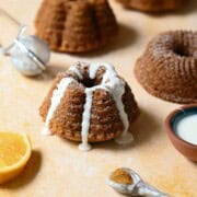 Mini mace bundt cake with white glaze on an orange surface.
