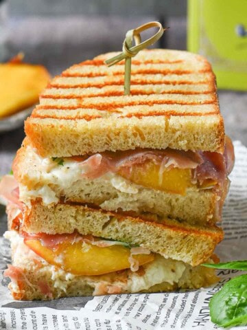 Peach panini stacked on del paper with basil and peaches in the background.
