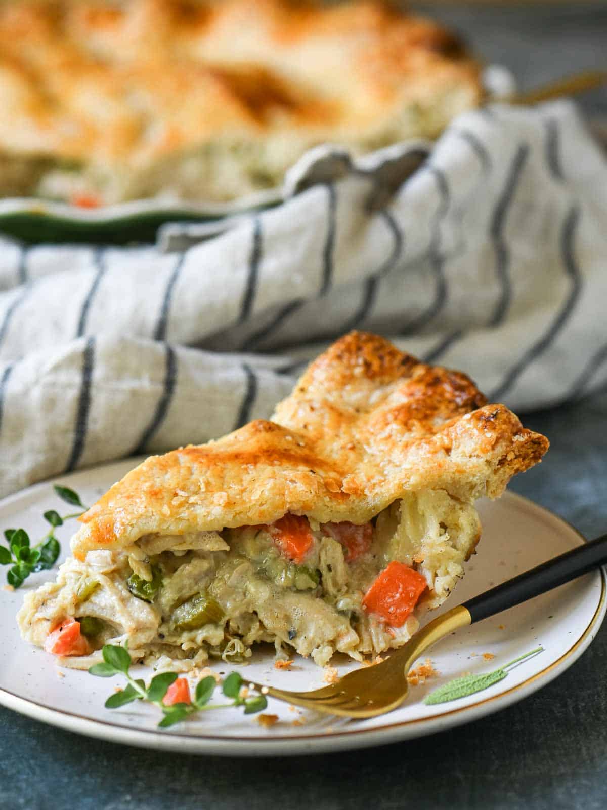 A slice of chicken pot pie on a white plate with herbs and a fork.