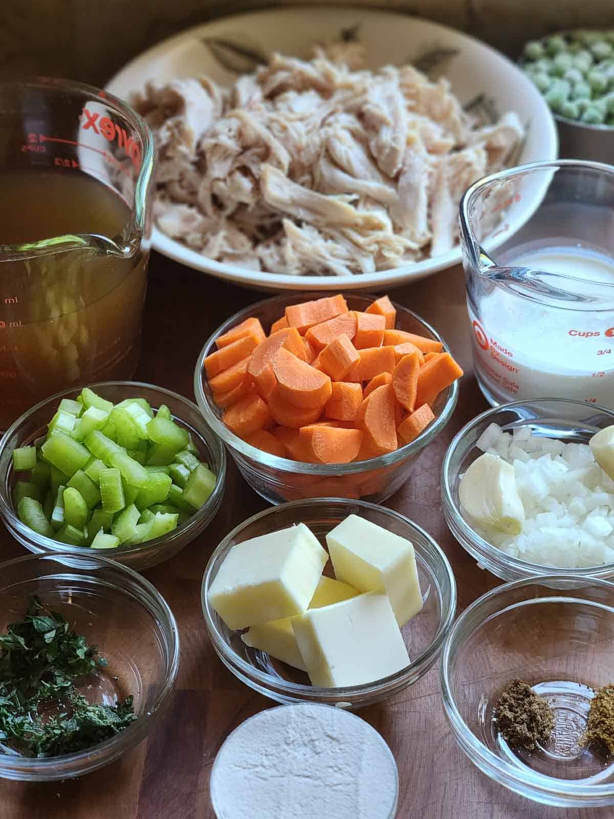 Ingredients for chicken pot pie filling in little bowls on a wood surface.