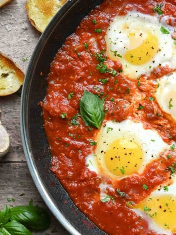 Overview of poached eggs in a skillet with tomato sauce with bread.