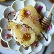 Overhead of poached pears in a flower plate with rose petals on top.