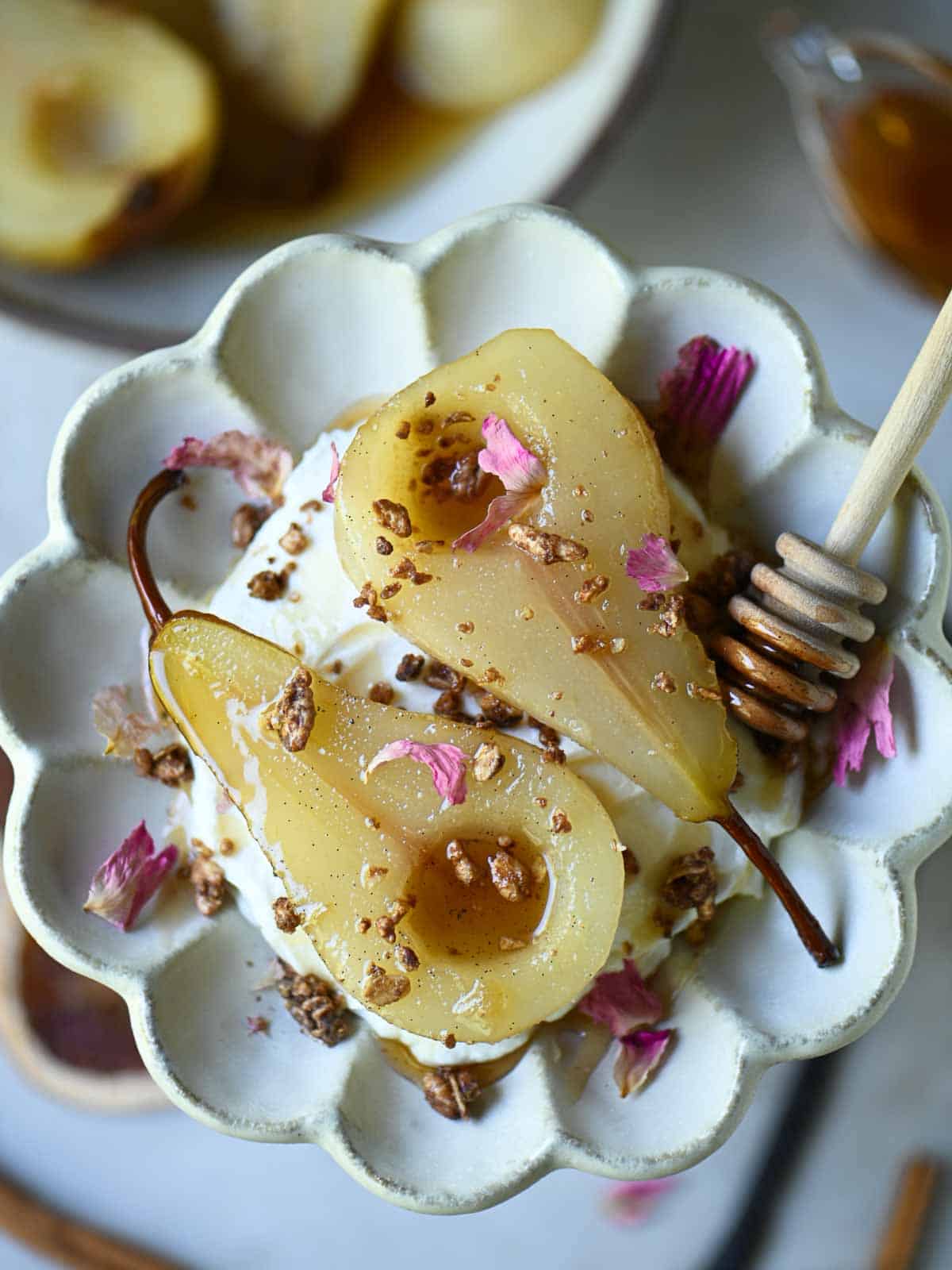 Overhead of poached pears in a flower plate with rose petals on top.
