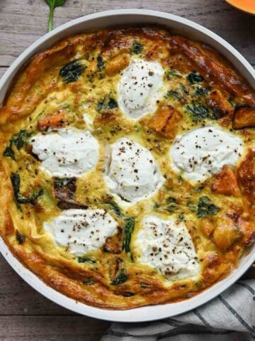 Overhead of a cooked frittata in a white skillet on a wood surface.