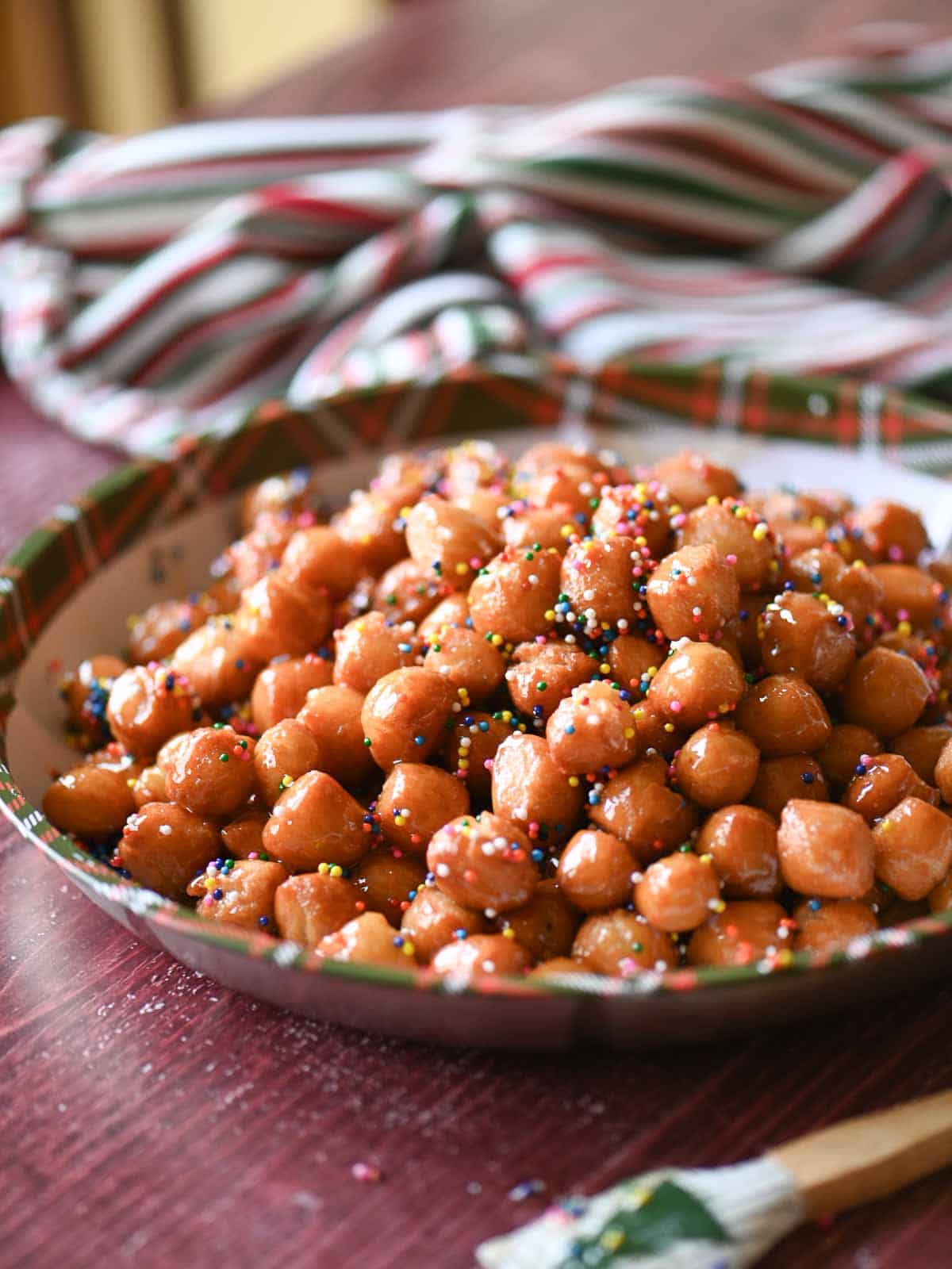 An angled view on honey balls in a tray on a red wooden surface.