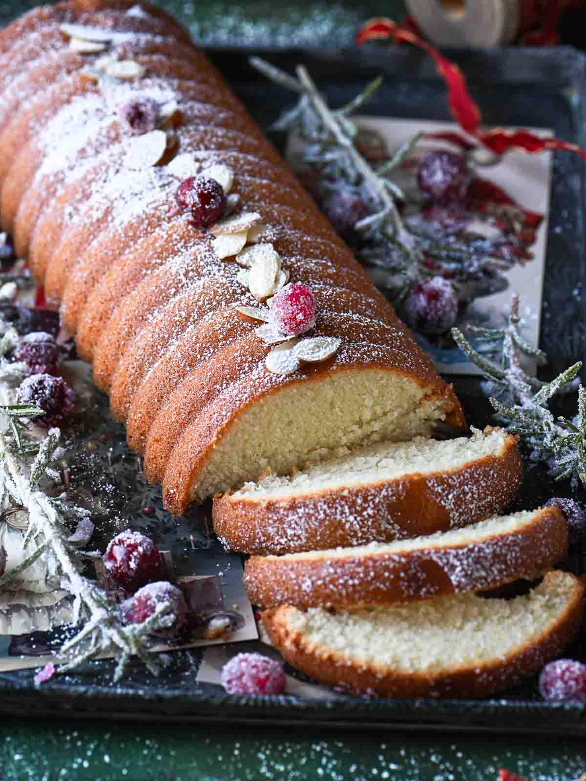 Angled view of almond cake with sugared cranberries and rosemary on the side.